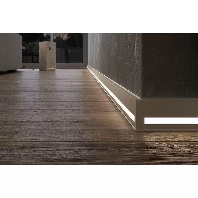 Deckprofil Cubica LS80 Light Down - Champagner, 2,5 m x 19 mm x 80 mm - Beleuchtete Sockelleisten entlang einer dunklen Wand und um eine Ecke, die den Holzboden dezent erhellen.