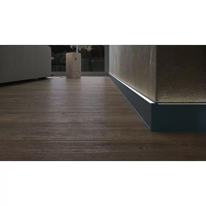 Deckprofil Cubica LS80 Light Up - Anthrazit, 2,5 m x 19 mm x 80 mm - Dunkelgraue Sockelleiste mit integrierter LED-Beleuchtung auf Holzboden, die die Wand beleuchtet.