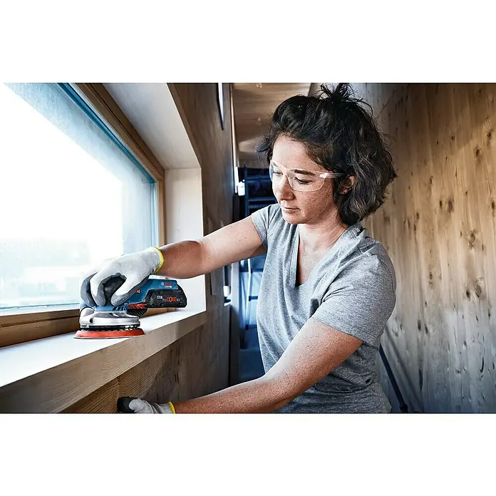 Bosch Professional AMPShare 18V Akku-Exzenterschleifer GEX 18V-125 - 18 V, Ohne Akku, Durchmesser Schleifteller: 125 mm, Karton - Frau schleift Holz mit einem Bosch Exzenterschleifer. Der handliche Schleifer ermöglicht flexibles Arbeiten dank Akkubetrieb und ergonomischem Design.