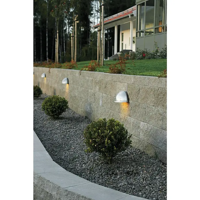 Konstsmide Außenwandleuchte - IP23, Edelstahl - Außenaufnahme einer Steinmauer mit eingelassenen Wandleuchten, die warmes Licht spenden und eine angenehme Atmosphäre erzeugen.
