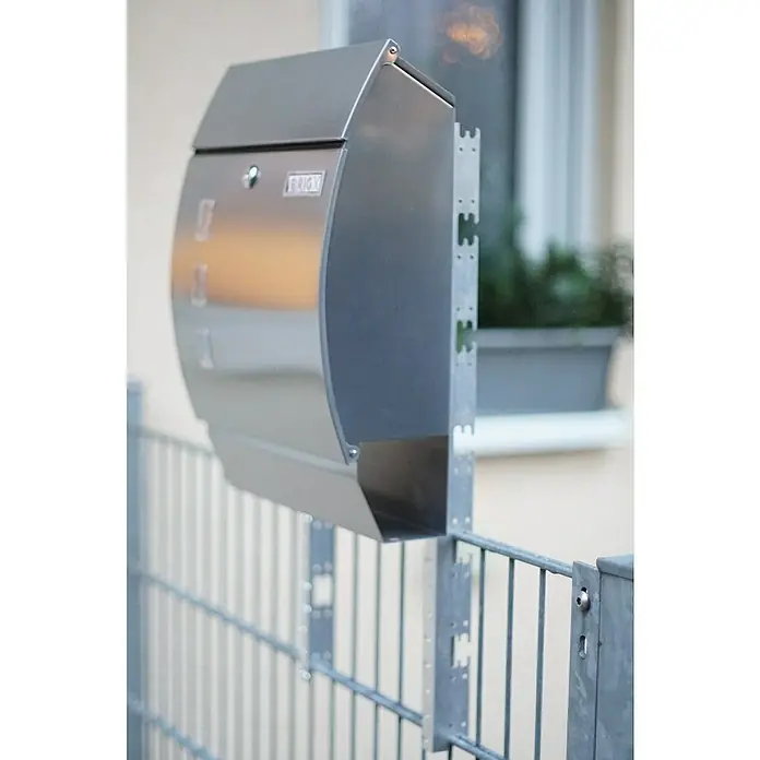 BRIGX Winkel - L x B x H: 596 x 40 x 20 mm, Passend für: Stabmatten - Moderner Briefkasten aus Edelstahl, montiert an einem grauen Metallzaun. Der Briefkasten ist schlank und hat ein schlichtes Design mit abgerundeten Kanten.