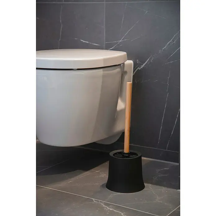 Wenko Bambusa WC-BürstengarniturBambus, Schwarz/Bambus - Eine Toilettenbürste mit Holzgriff und schwarzem Behälter steht neben einer Toilette in einem Badezimmer mit grauen Fliesen.