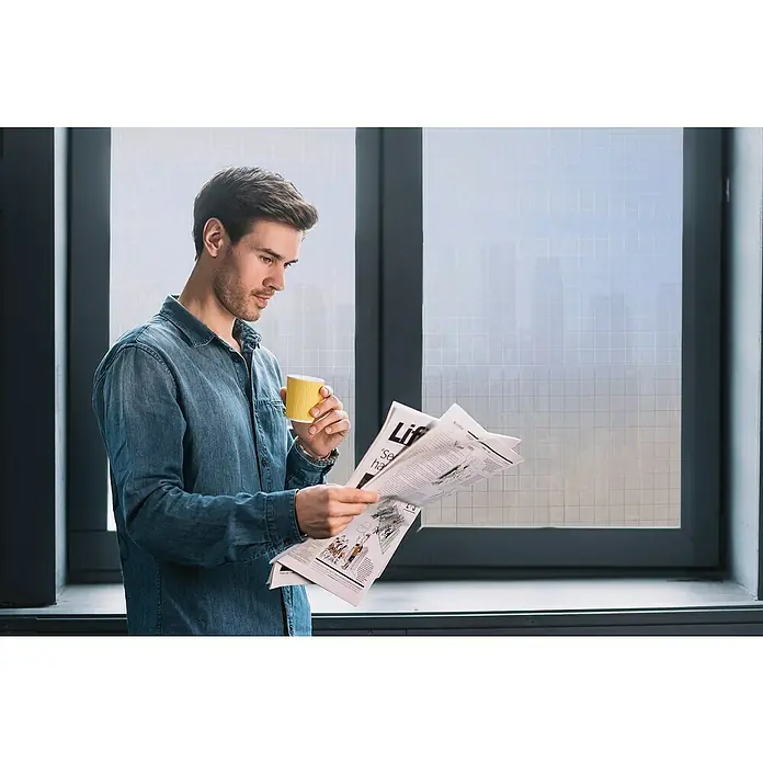 Lámina para ventana al corte Linea Fix Check - Transparente - Un hombre lee un periódico y sostiene una taza amarilla mientras está de pie junto a una ventana.