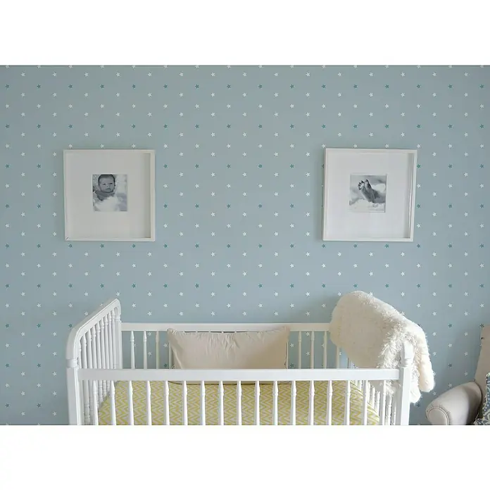 Papel pintado de vinilo autoadhesivo Daniela - 90 cm x 3 m, 100% PVC, Aqua - Primer plano de una cuna blanca con una manta amarilla en una habitación infantil con estrellas y marcos en la pared.