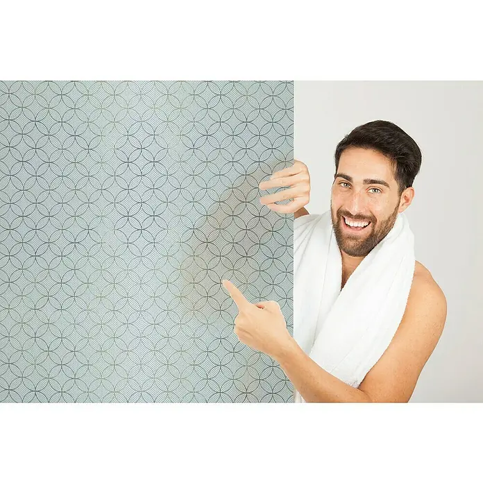 Lámina para ventana gofrado Fix rissani mini - 46 cm x 1,5 m, Transparente - Un hombre en albornoz muestra un vinilo decorativo para ventanas con un elegante patrón circular, perfecto para privacidad y estilo.