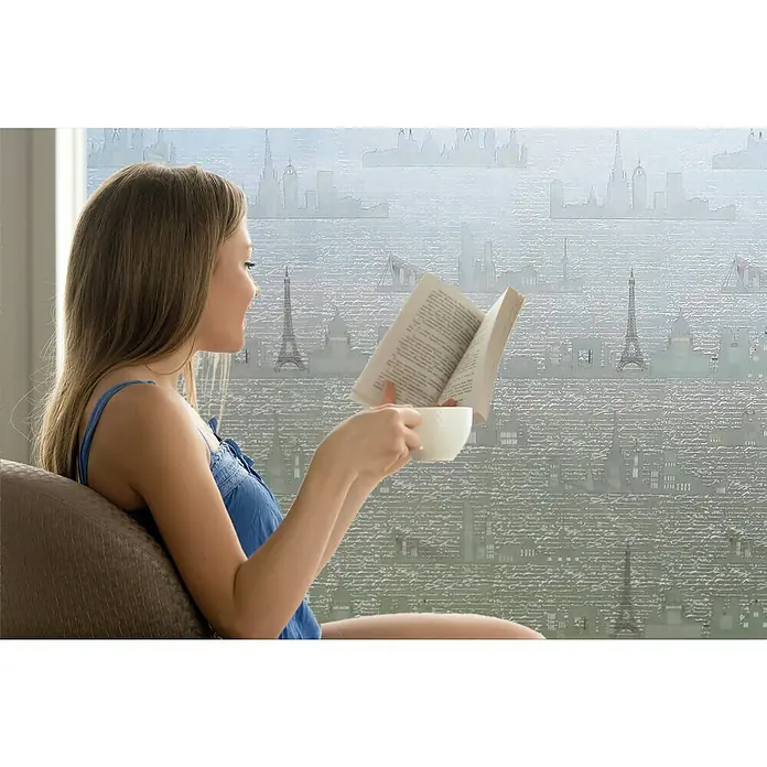 Lámina para ventana al corte estampado fix Travelling - Transparente - Mujer leyendo un libro frente a una ventana con un papel tapiz de horizonte. Disfruta de un momento tranquilo con una taza en la mano.