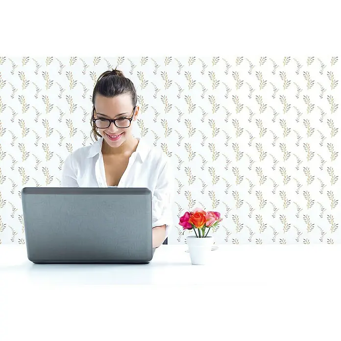 Papel pintado de vinilo autoadhesivo Ramas - 90 cm x 3 m, 100% PVC - Una mujer trabaja en su computadora portátil con una maceta con rosas coloridas en la mesa frente a un fondo elegante.