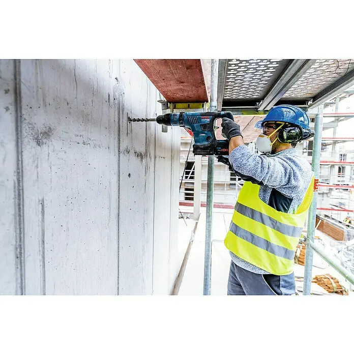 Bosch Professional AMPShare 18V Akku-Kombihammer GBH 18V-36 C - 18 V, 2 Akkus, 8 Ah, 7 J - Bauarbeiter bohrt mit einer Bosch-Bohrmaschine ein Loch in eine Betonwand auf einer Baustelle, wobei er Sicherheitsausrüstung trägt.