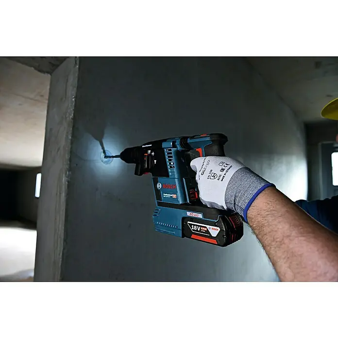 Bosch Professional AMPShare 18V Akku-Kombihammer GBH 18V-26 F - 18 V, 2 Akkus, 5,5 Ah, 2,6 J, Inkl. Staubabsaugung - Ein Arbeiter bohrt mit einem Bosch Akku-Bohrhammer ein Loch in eine Betonwand. Ideal für Bauprojekte und Renovierungsarbeiten.