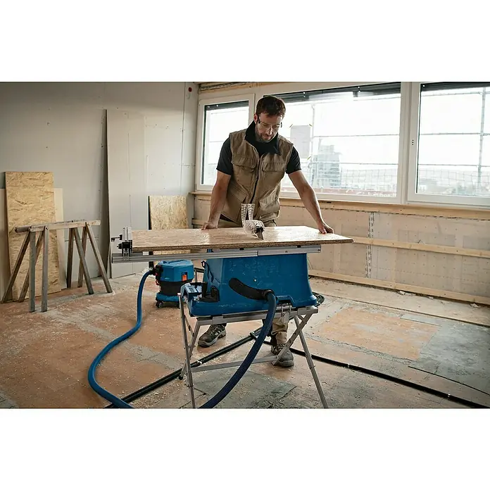 Bosch Professional AMPShare 18V Akku-Tischkreissäge GTS 18V-216 - 18 V, Ohne Akku, Durchmesser Sägeblatt: 216 mm, Ohne Sägetisch - Ein Mann arbeitet mit einer blauen Tischkreissäge mit Absaugvorrichtung, um ein Holzbrett zuzuschneiden.