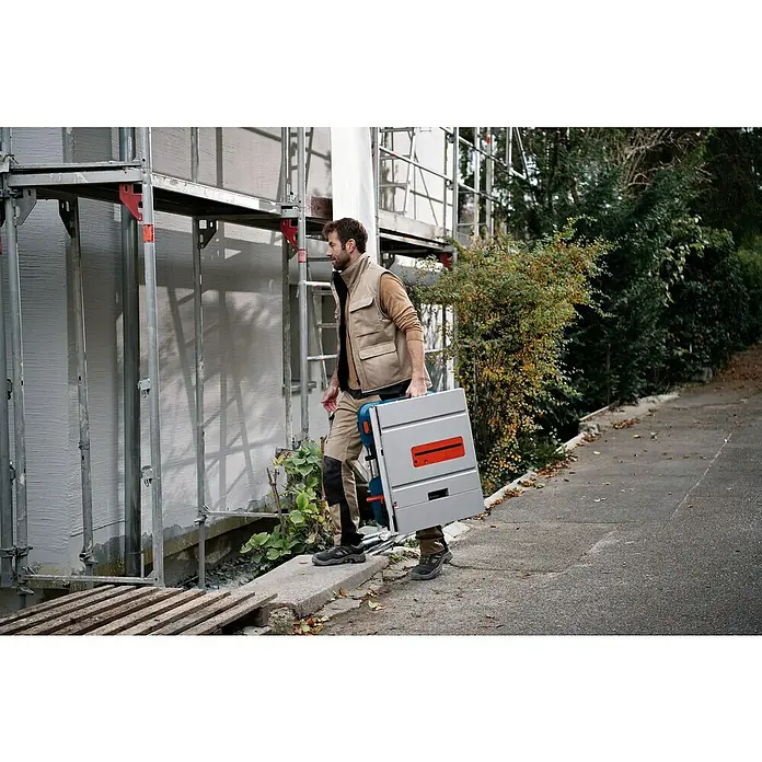 Bosch Professional AMPShare 18V Akku-Tischkreissäge GTS 18V-216 - 18 V, Ohne Akku, Durchmesser Sägeblatt: 216 mm, Ohne Sägetisch - Mann trägt Bosch-Tischsäge Baustelle entlang.