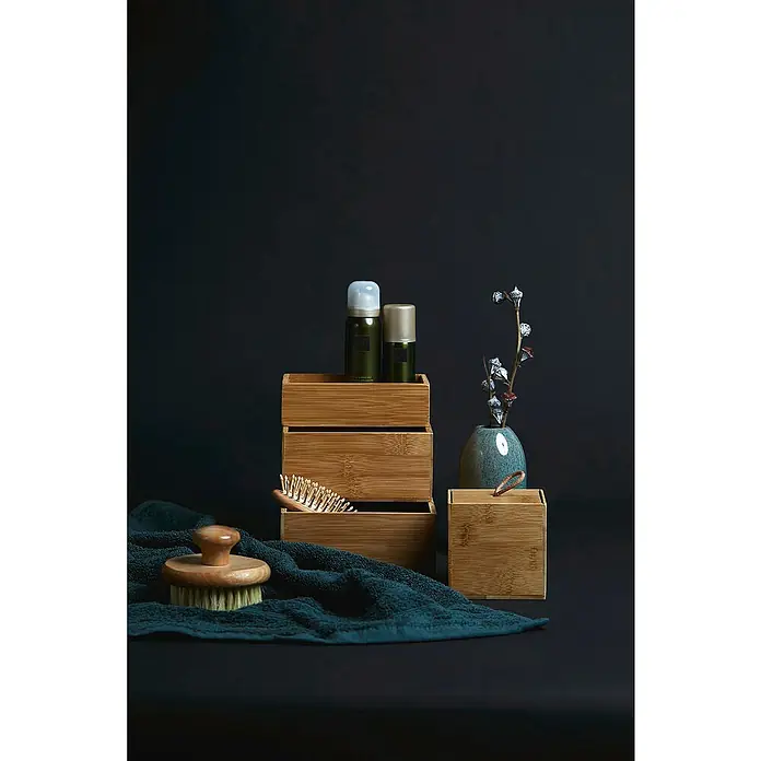 Wenko Aufbewahrungsbox Terra L - 15 x 22 x 7 cm, Bambus - Produktstillleben mit Holzboxen, Hautpflegeprodukten, Bürsten und einem Handtuch vor dunklem Hintergrund.