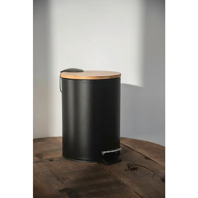 Wenko Kosmetikeimer Tortona - 3 l, Stahl, Schwarz/Bambus - Ein eleganter, schwarzer Treteimer mit einem Deckel aus hellem Holz steht auf einem rustikalen Holztisch.