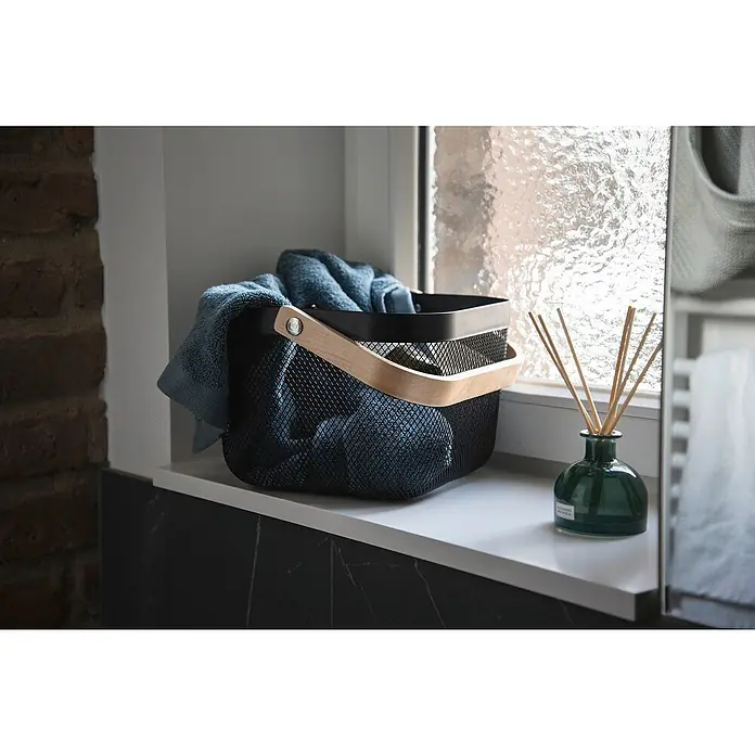 Wenko Bambusa Bad-Aufbewahrungskorb25 x 25 x 17 cm, Stahl, Schwarz/Bambus - Korb mit Handtuch und Aroma Diffuser. Der Korb ist aus schwarzem Metall mit einem Holzgriff und einem Handtuch darin.