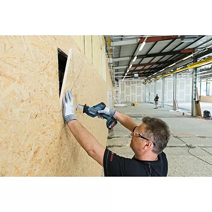 Bosch Professional AMPShare 18V Akku-Säbelsäge GSA 18V-LI - 18 V, Ohne Akku - Eine Person schneidet mit einer blau-schwarzen Bosch Professional Akku-Säbelsäge ein Loch in eine OSB-Wandplatte auf einer Baustelle.
