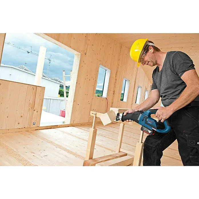 Bosch Professional AMPShare 18V Akku-Säbelsäge GSA 18V-32 - 18 V, Ohne Akku, 0 /min - 2.500 /min, Karton - Ein Handwerker in Arbeitskleidung sägt mit einer Bosch Säbelsäge ein Holzstück, während er in einem unfertigen Holzhaus arbeitet.