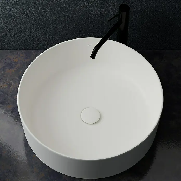 RAK Ceramics Feeling Ablaufventil - 1 ¼″, Weiß, Permanent geöffnet - Nahaufnahme eines runden, weißen Aufsatzwaschbeckens mit schwarzer Armatur auf einer dunklen Arbeitsplatte.