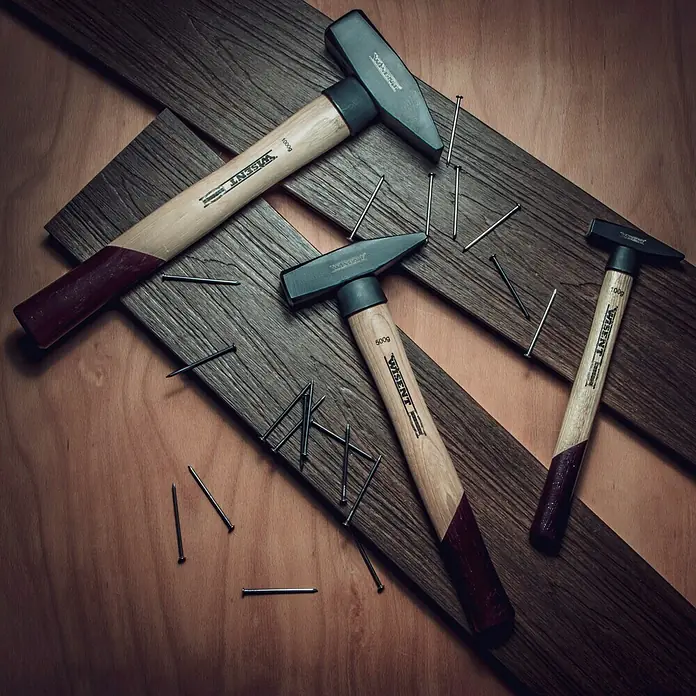 Wisent Schlosserhammer - 100 g, Holz Hickory - Drei WISENT Hämmer unterschiedlicher Größe und Nägel liegen auf Holzbrettern. Ideal für Heimwerker und Profis.
