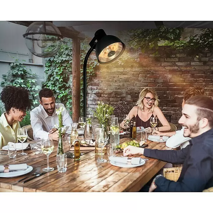 Hoberg Infrarot-Heizstrahler - Schwarz - Ein schwarzer Stand-Terrassenheizer beleuchtet einen Esstisch im Freien mit mehreren Personen.