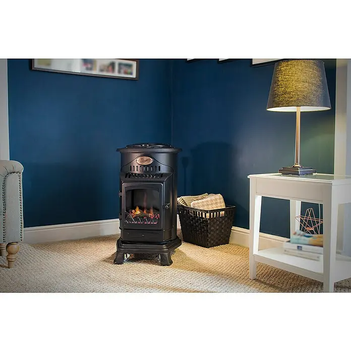 Estufa de gas Provence - 3,4 kW, Negro - Un primer plano de un calentador negro portátil junto a una mesa auxiliar blanca con una lámpara y una canasta en una habitación acogedora.