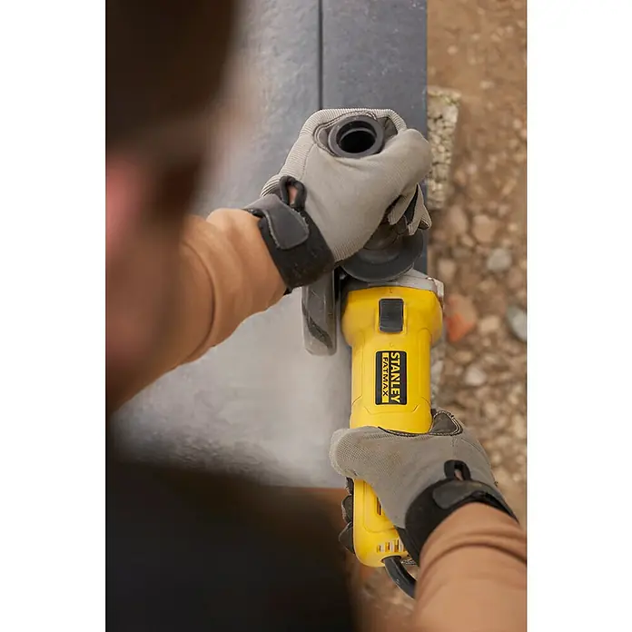 Stanley FatMax Amoladora angular eléctrica FMEG615-QS - 600 W, Diámetro disco: 115 mm, Número de revoluciones de marcha en vacío: 12.000 r.p.m. - Primer plano de una amoladora angular amarilla Stanley Fatmax que está siendo utilizada por una persona con guantes para rectificar una superficie.
