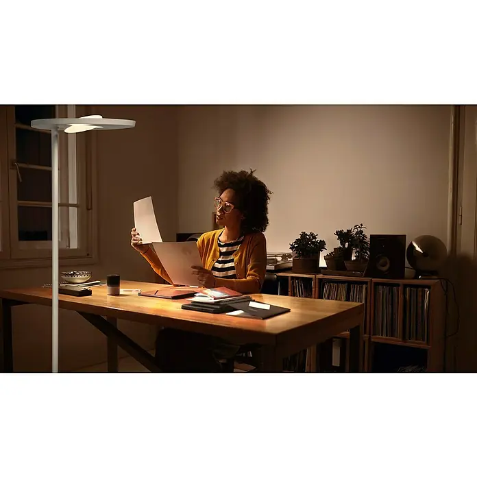 Ledvance SUN@Home LED-Stehleuchte Panan - 36 W, Höhe: 180 cm, Weiß, Kaltweiß - Frau liest unter einer modernen Stehlampe, die helles Licht spendet. Die Lampe ist schlank und minimalistisch designt.