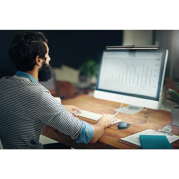 Ledvance SUN@Home Bürobeleuchtung - Breite: 4,4 cm - Ein Mann arbeitet am Computer mit einer praktischen Monitorlampe, die für blendfreies Licht sorgt und die Augen schont. Perfekt für lange Arbeitstage.
