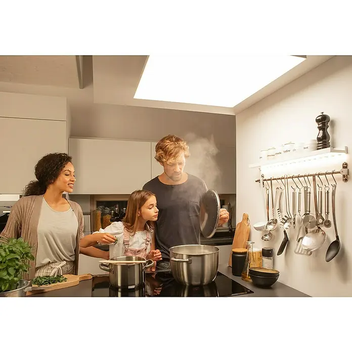 Ledvance SUN@Home LED-Panel Planon Frameless - 20 W, L x B x H: 30 x 30 x 6,1 cm, Weiß, Kaltweiß - Eine Familie kocht gemeinsam in einer modernen Küche, Dampf steigt aus den Töpfen. Die Küchenutensilien hängen ordentlich an der Wand.