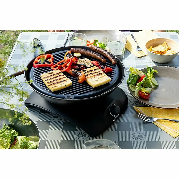 Campingaz Barbacoa de gas CV 360 - 2.400 W, Número de quemadores: 1 - Una parrilla Campfire con comida a la parrilla, incluyendo halloumi, salchicha y pimientos, en una mesa con ensaladas y bebidas.