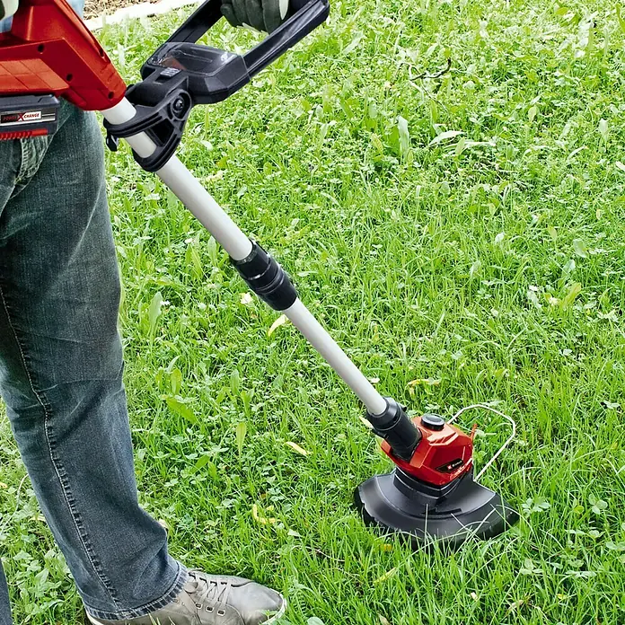 Einhell Power X-Change 18V Akku-Rasentrimmer GE-CT 18 Li-Solo - 18 V, Li-Ionen, Ohne Akku - Eine Person benutzt einen Rasentrimmer der Marke Einhell, um Gras zu schneiden. Der Trimmer ist rot und schwarz.