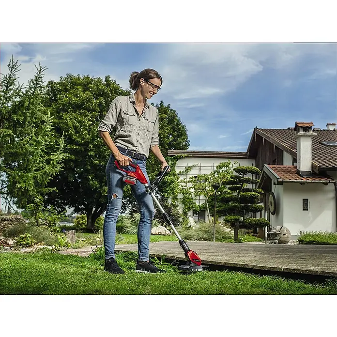 Einhell Power X-Change 18V Akku-Rasentrimmer GE-CT 18 Li-Solo - 18 V, Li-Ionen, Ohne Akku - Eine Frau benutzt einen Rasentrimmer, um Gras an einer Holzterrasse zu schneiden. Der Rasentrimmer ist rot und schwarz.