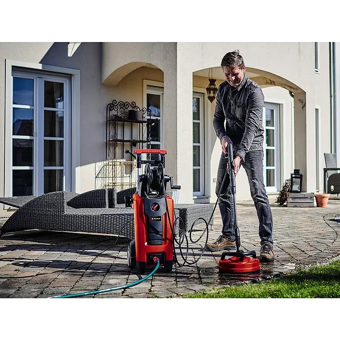 Einhell Hochdruckreiniger TE-HP 170 - 2.300 W, Max. Druck: 170 bar, Fördermenge: 440 l/h - Ein Mann benutzt einen Einhell Hochdruckreiniger mit Flächenreiniger, um eine Terrasse zu reinigen. Das Gerät ist rot-schwarz und steht auf Steinplatten.