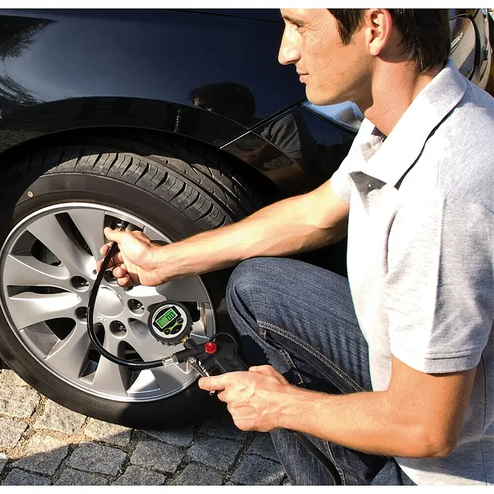 Einhell Reifenfüllmesser digital - Betriebsdruck: 13 bar - Eine Person überprüft den Reifendruck mit einem digitalen Reifendruckmessgerät an einem schwarzen Auto. Das Gerät zeigt 0,0 PSI an.