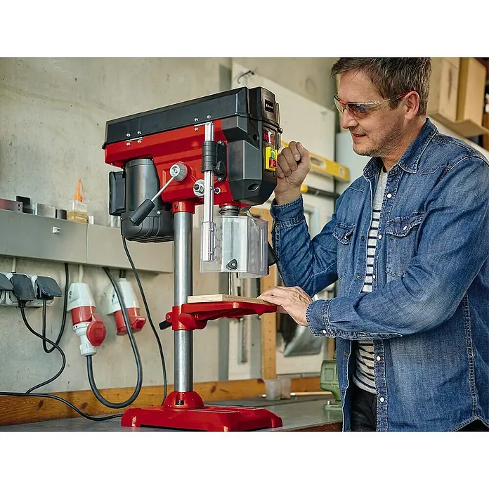 Einhell Tischbohrmaschine TE-BD 550 E - 450 W, Spannweite Bohrfutter: 0 mm - 13 mm - Der Mann bedient eine rote Einhell Tischbohrmaschine in einer Werkstatt, er trägt Schutzbrille und eine blaue Jeansjacke.