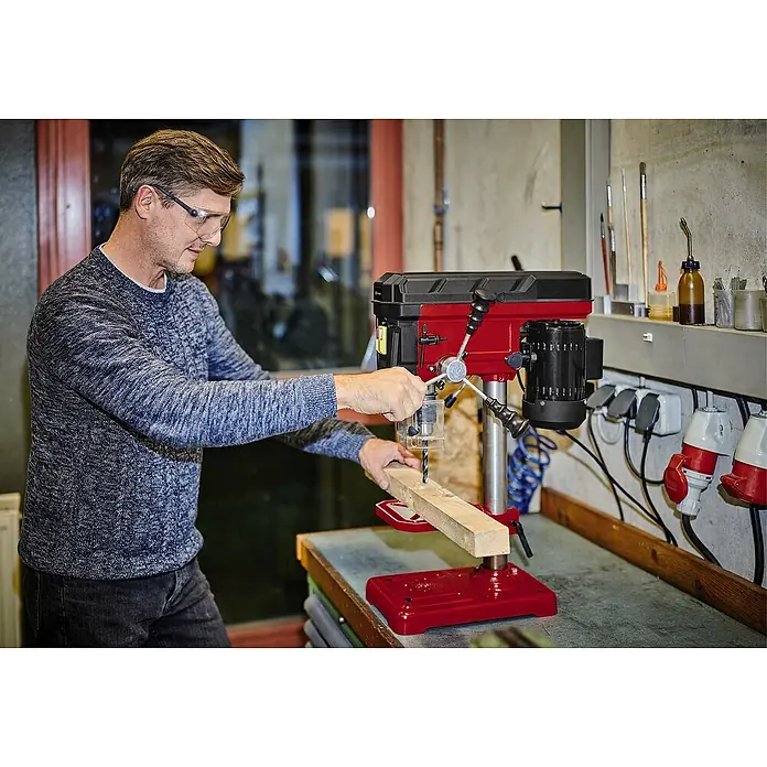 Einhell Classic Tischbohrmaschine TC-BD 500 - 500 W, Leerlaufdrehzahl: 300 U/min - 2.410 U/min, Spannweite Bohrfutter: 1,5 mm - 13 mm - Ein Mann bedient eine rote Tischbohrmaschine in einer Werkstatt, um präzise Löcher in ein Holzstück zu bohren.