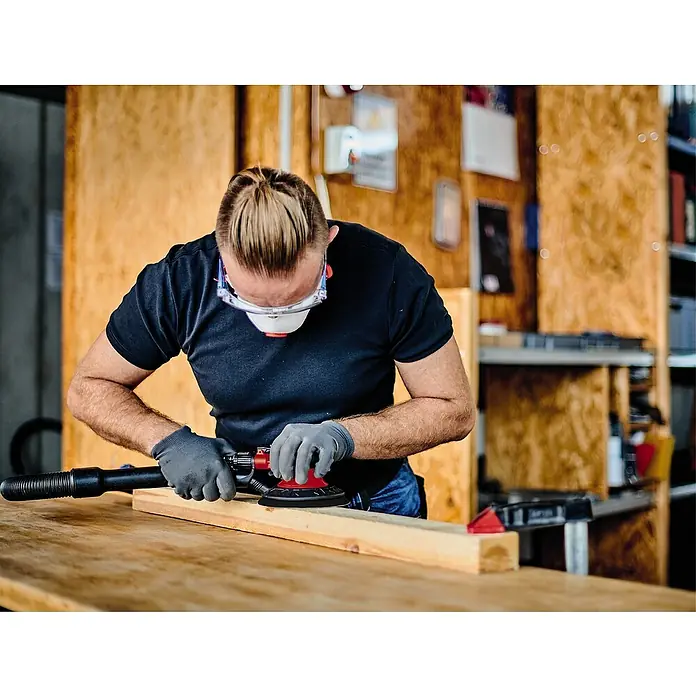 Einhell Classic Druckluft-Exzenterschleifer TC-PE 150Durchmesser Schleifteller: 150 mm, 10.500 U/min, 0 bar - 6,3 bar - Mann schleift ein Holzbrett mit einem Exzenterschleifer, Schutzbrille und Atemschutzmaske für sicheres und effizientes Arbeiten.