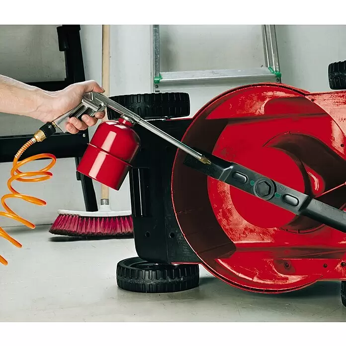 Einhell Druckluft-Set - 5 -tlg. - Eine Hand reinigt mit einer silber-roten Sprühpistole und orangefarbenem Schlauch die rote Unterseite eines Rasenmähers.