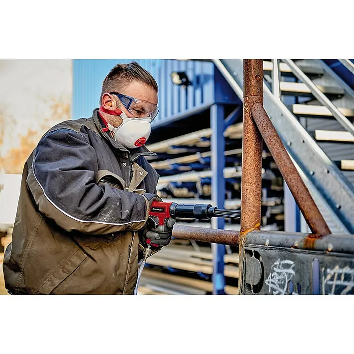 Einhell Classic Druckluft-Meißelhammer - 6,3 bar, Luftverbrauch: 113 l/min, Schlagzahl: 4.500 /min - Ein Mann benutzt einen Einhell Druckluft-Nadelentroster zum Entfernen von Rost, wobei er Schutzausrüstung trägt.