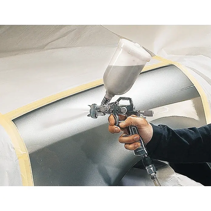 Einhell Druckluft-Farbspritzpistole Profi - 0,6 l, 3 bar - 3,5 bar - Nahaufnahme einer Person, die mit einer Spritzpistole ein silbernes Objekt besprüht, was die präzise Anwendung und Verarbeitung von Lacken hervorhebt.