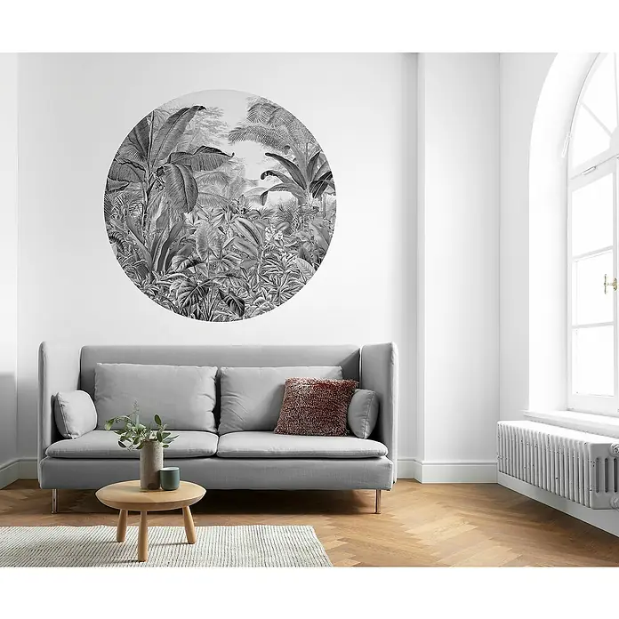 Komar Dots Fototapete rund Wild Woods - 128 cm, Selbstklebend - Ein stilvolles Wohnzimmer mit einem grauen Sofa, einem runden Dschungel-Wandbild und einem Holztisch auf einem Teppich. Helles Interieur.