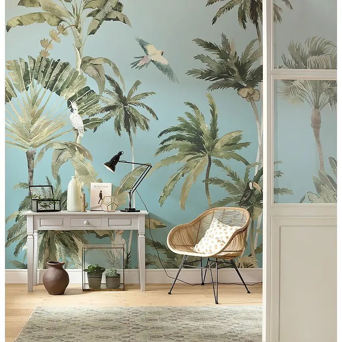 Komar Fototapete Forêt de PalmiersB x H: 300 x 250 cm, Vlies - Elegantes Interieur mit einem Schreibtisch und einem Rattansessel vor einer Wand mit Palmenmuster, die ein tropisches Ambiente schafft.