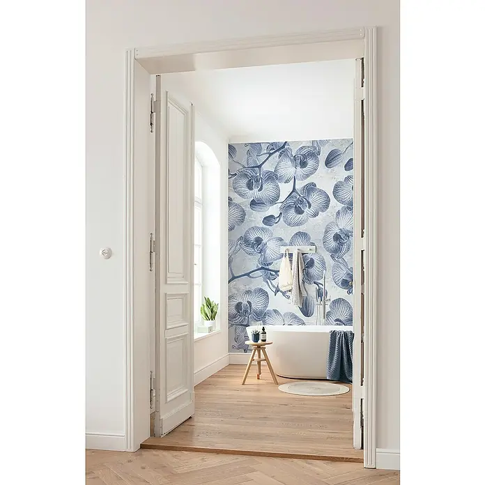 Komar Fototapete Orchidee - B x H: 200 x 250 cm, Vlies - Ein Badezimmer mit einer Badewanne vor einer Wand mit blauem Orchideenmuster, aufgenommen durch eine geöffnete Tür.