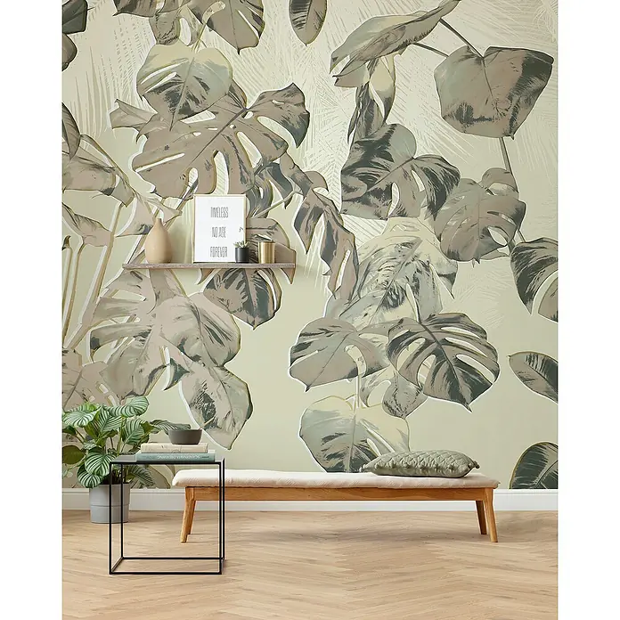Komar Fototapete Tresor - B x H: 350 x 250 cm, Vlies - Nahaufnahme eines Zimmers mit einem Wandgemälde von grünen Blättern, einem Holztisch und einer Zimmerpflanze.
