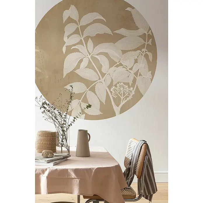 Komar Dots Fototapete rund Blooming Branch - 128 cm, Selbstklebend - Elegantes Interieur mit einem Tisch bedeckt mit einer rosa Tischdecke, einer Vase und einem Korb, vor einer Wandmalerei mit floralem Motiv.