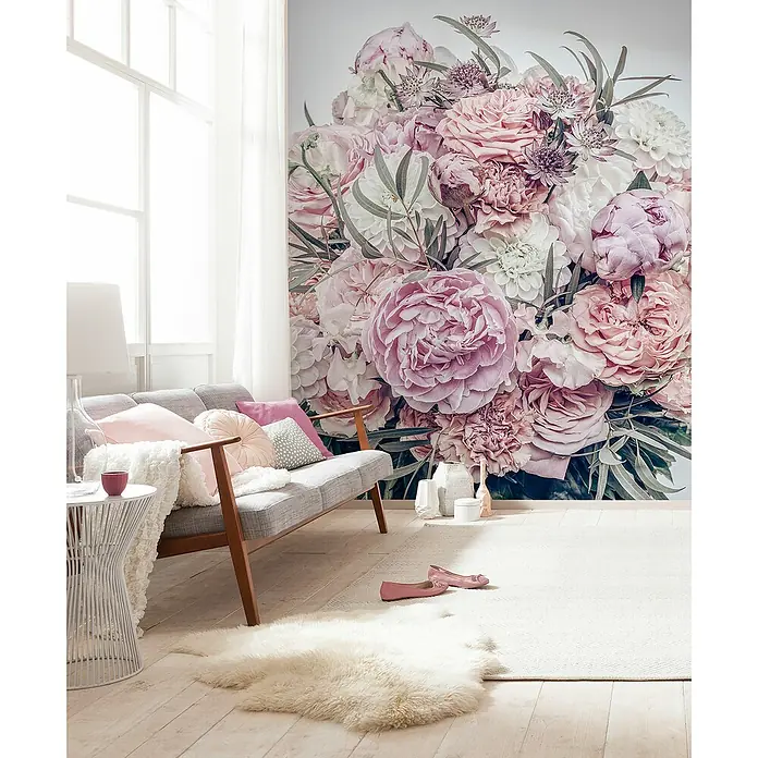 Komar Fototapete ZestfulB x H: 200 x 250 cm, Vlies - Ein Wohnzimmer mit einem grauen Sofa, rosa Kissen und einem weißen Teppich, vor einer floralen Wandtapete.