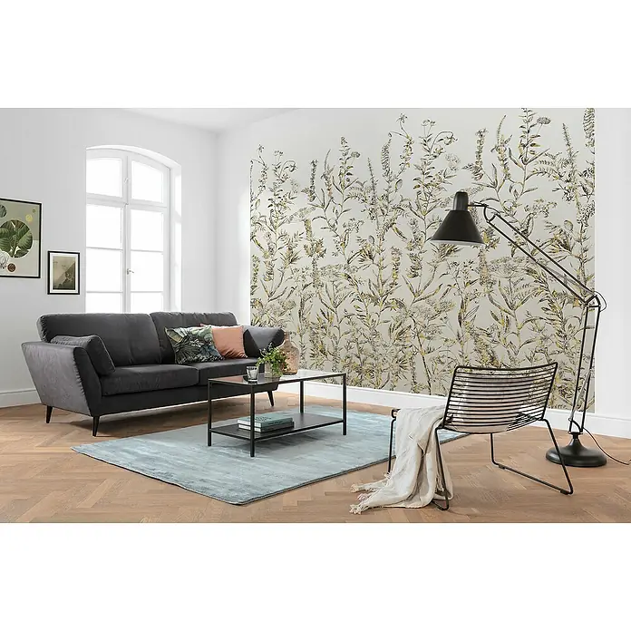 Komar Fototapete Eldorado - B x H: 300 x 250 cm, Vlies - Wohnzimmer mit anthrazitfarbenem Sofa, Couchtisch und Stehlampe vor einer floralen Tapete, die eine gemütliche Atmosphäre schafft.