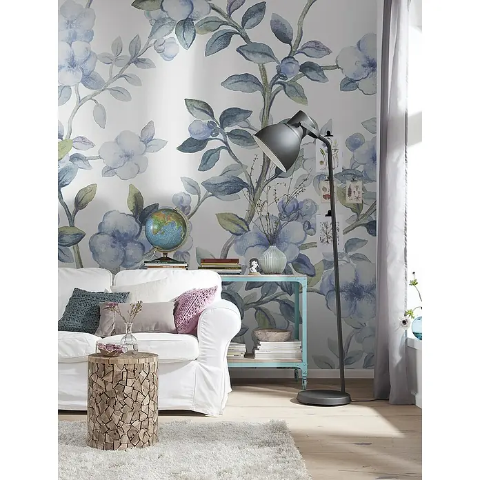 Komar Fototapete Bleu Ciel - B x H: 200 x 250 cm, Vlies - Wohnzimmer mit weißem Sofa, Holzhocker und Stehlampe vor einer blumigen Wand. Die Stehlampe bietet optimales Licht für den Raum.