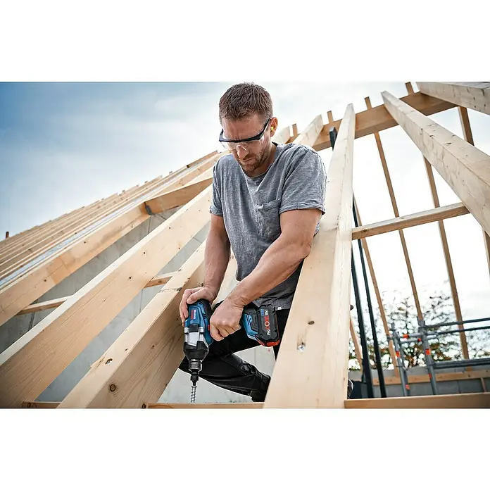 Bosch Professional AMPShare 18V Akku-Drehschlagschrauber GDS 18V-1000 C - 18 V, 2 Akkus, 8 Ah, 1.000 Nm, Inkl. Bluetooth Low Energy Modul GCY 42 - Ein Handwerker befestigt mit einem Bosch Akku-Schlagschrauber PROFACTOR 18V eine Schraube in einem Holzrahmen. Er trägt dabei eine Schutzbrille.
