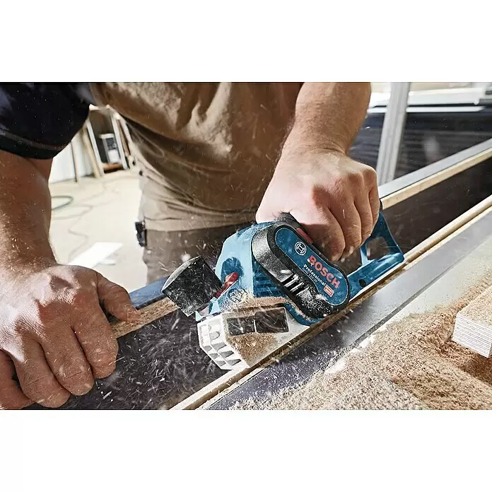 Bosch Professional Akku-Handhobel GHO 12V-20 - 12 V, Li-Ionen, Ohne Akku, Hobelbreite: 56 mm - Eine Person benutzt einen blau-schwarzen Bosch Professional Hobel zum Glätten von Holz, wobei Späne entstehen.