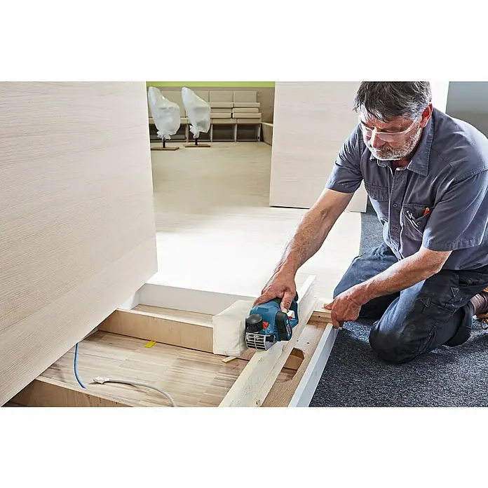 Bosch Professional Akku-Handhobel GHO 12V-20 - 12 V, Li-Ionen, Ohne Akku, Hobelbreite: 56 mm - Ein Handwerker benutzt einen Bosch Elektrohobel, um Holz anzupassen, wobei er eine Schutzbrille trägt.